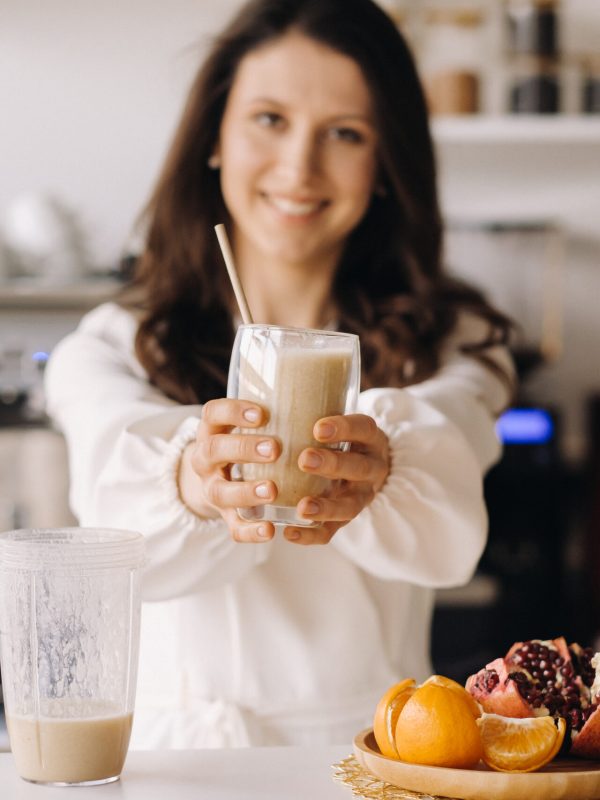 A happy smiling healthy woman has prepared a fruit cocktail and gives it to you while standing at home in the kitchen.Healthy eating.