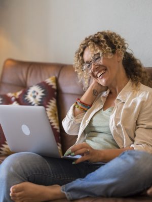Adult woman sit down on the sofa at home enjoy video call conference with friends smiling and speaking on laptop computer - online people and wireless connection